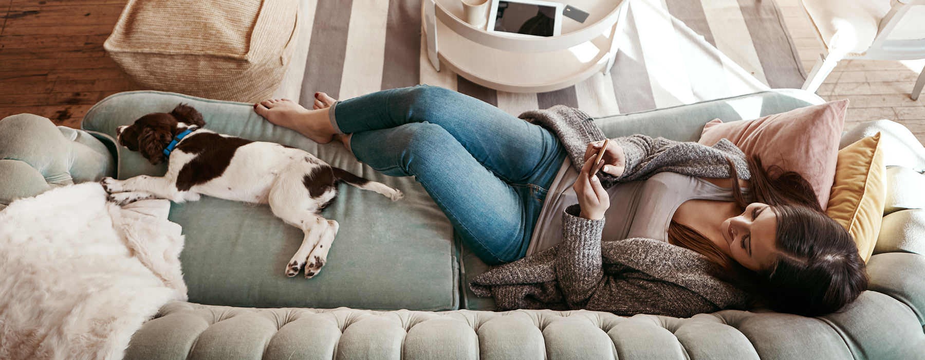 woman texts while lying on a couch next to her dog